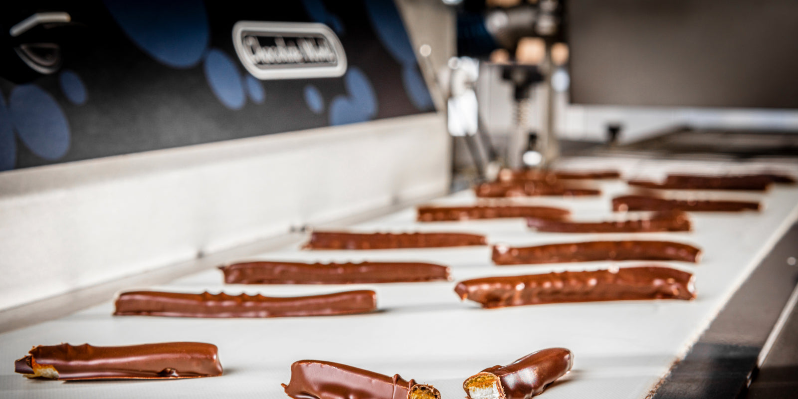 Chocolate World Belgium enrobing machine coating chocolate bars on industrial conveyor belt in professional production line